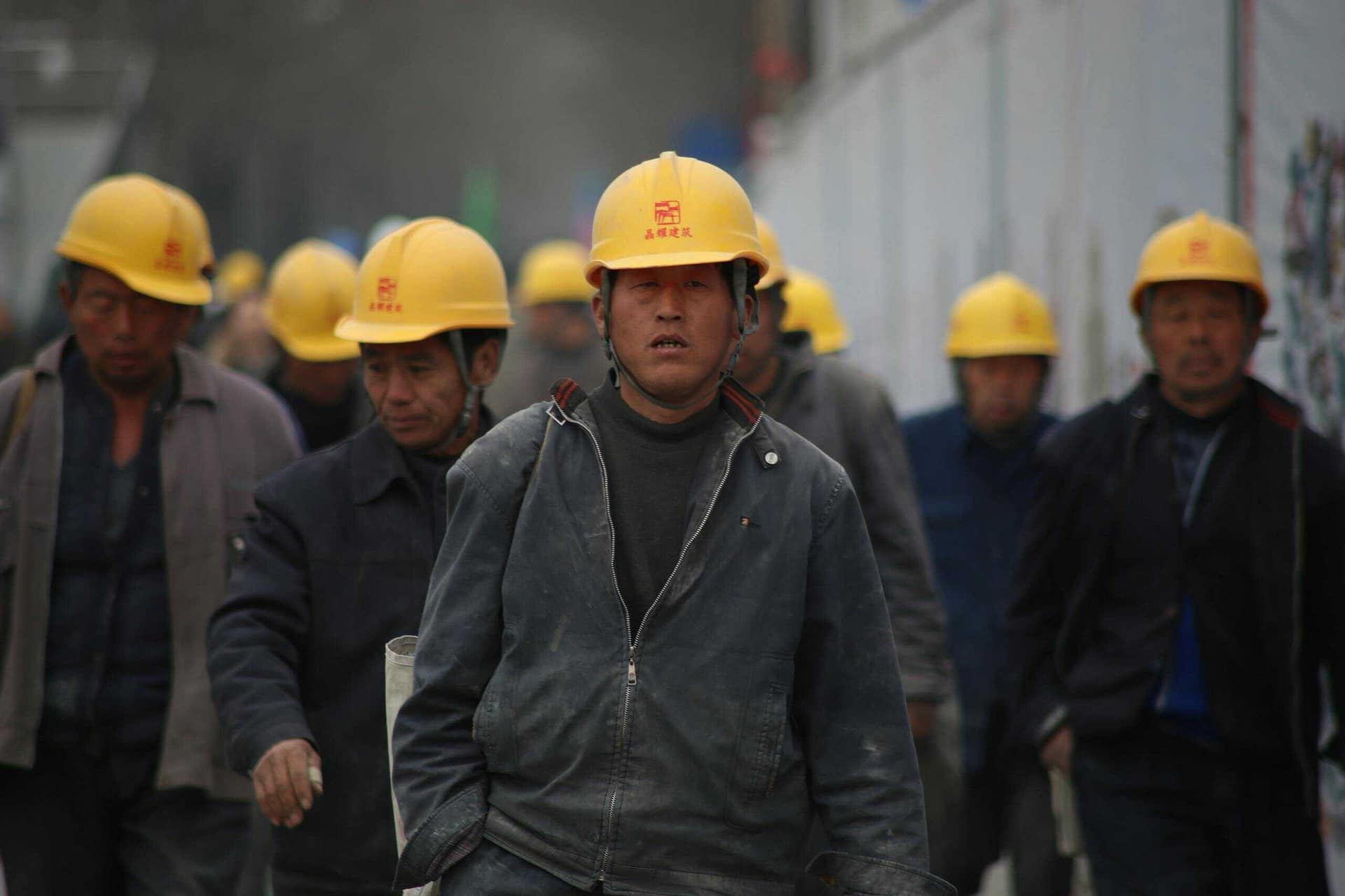 Muncitori în construcții cu căști de protecție mergând pe un șantier, subliniind munca în echipă și siguranța